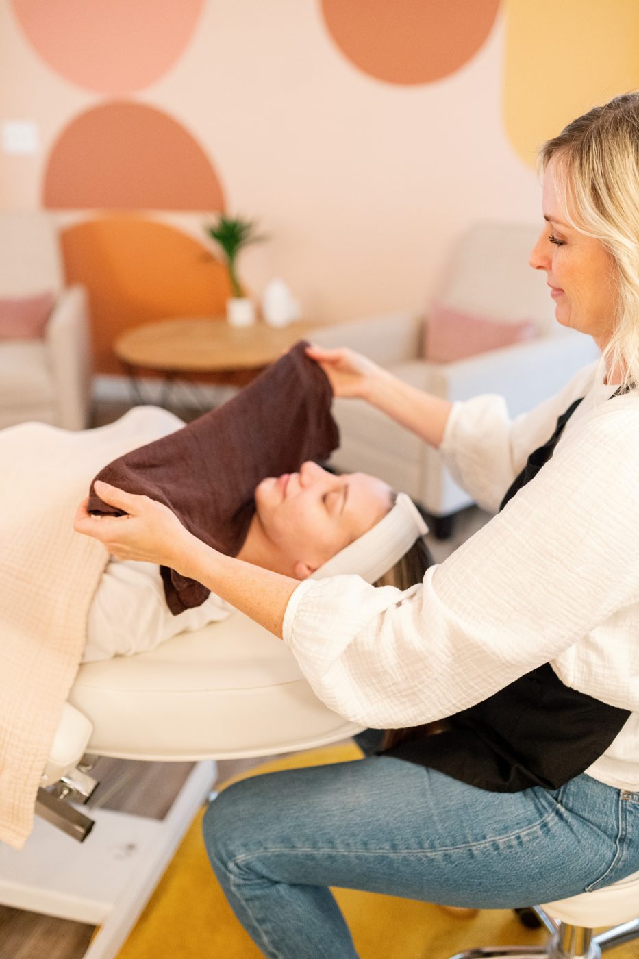 An esthetician finishes a treatment with a warm towel in the Mia June lounge